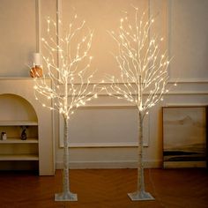 two white lighted trees in the middle of a room with wood flooring and walls