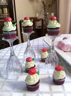 cupcakes with white frosting and cherries in wine glasses on a table