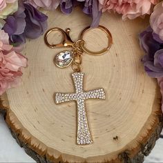 a cross keychain is sitting on a piece of wood with flowers around it