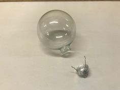 a small glass object sitting on top of a white table next to a tiny silver object