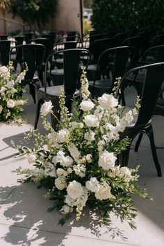 white flowers and greenery are on the ground in front of rows of black chairs