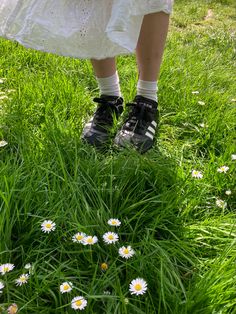 a woman in white dress and black shoes standing on grass with daisies