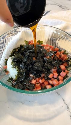 someone pouring sauce into a bowl filled with food on top of a marble countertop