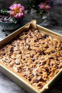 a pan filled with chocolate chip cookie bars on top of a marble counter next to flowers