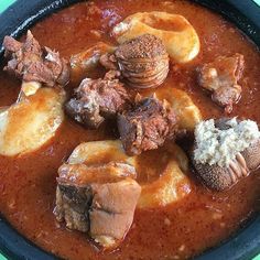 a bowl filled with stew and meats on top of a green tablecloth covered table