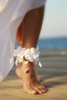 a barefoot woman's foot with white flowers on it and the ocean in the background