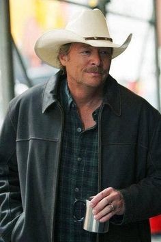 a man wearing a cowboy hat and holding a drink in his hand while walking down the street