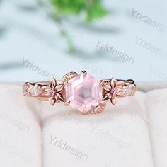 an engagement ring with a pink stone surrounded by white and rose gold leaves on the band