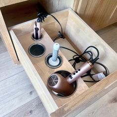 an open drawer with hair dryers and other items in it on the floor next to a wooden cabinet