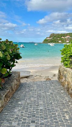 a stone walkway leading to the beach with boats in the water