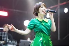 a woman in a green dress holding a microphone and singing into the air on stage