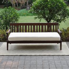 a wooden bench sitting on top of a rug in front of a tree and bushes