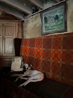 a white dog laying on top of a bed next to a dresser and painting above it