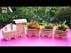 wooden toy train with flowers in it on a pink table next to green plants and trees