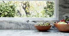 two wooden bowls filled with different types of fruits and vegetables sitting on a marble counter top