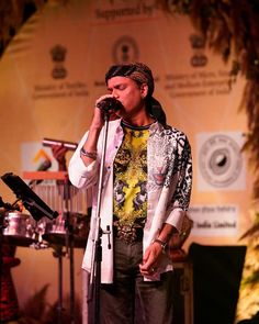 a man singing into a microphone while standing in front of a stage with other instruments