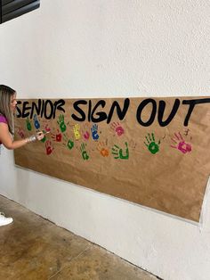 a woman painting a sign that says senior sign out with handprints on it