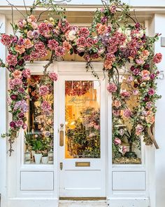 a white door with pink flowers hanging over it's glass front entrance to a flower shop