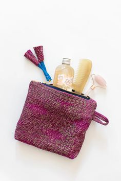 a purple bag with some hair products in it on a white surface next to other items