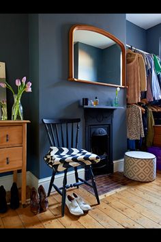 a room with a chair, mirror and shoes on the floor in front of a fireplace