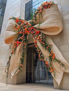 a large bow decorated with orange flowers and greenery on the outside of a building