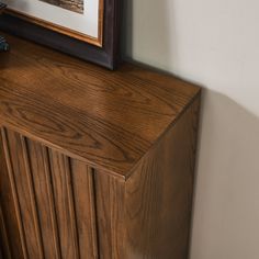 a wooden cabinet with a painting on the wall behind it and a framed photograph above it