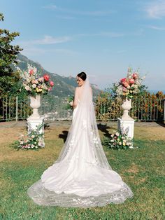 a woman in a wedding dress standing on the grass with flowers and greenery behind her