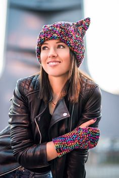 a woman wearing a knitted hat and leather jacket with her arms crossed in front of her chest