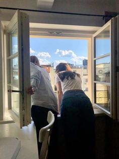 two people standing in front of an open window