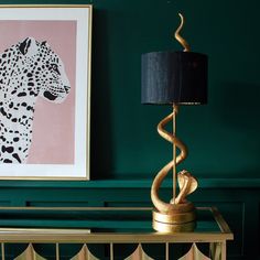 a gold table with a black lamp on top and a leopard painting above it in a green room