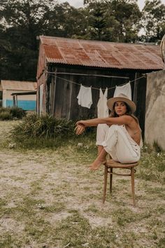 a woman sitting on top of a wooden chair in front of a building with clothes hanging out to dry