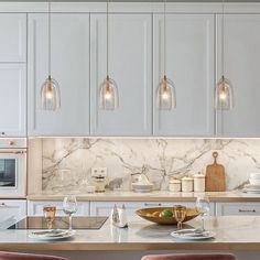 a kitchen with marble counter tops and white cabinets, along with wine glasses on the bar