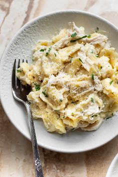 a white plate topped with pasta covered in chicken and parsley next to a fork