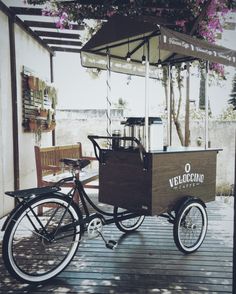 a bicycle with a cart attached to it parked on a wooden deck next to a bench