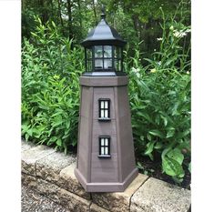 a small gray light house sitting on top of a stone wall next to green plants