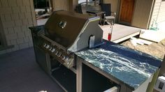 an outdoor grill with blue marble counter tops and stainless steel doors on the outside of a house