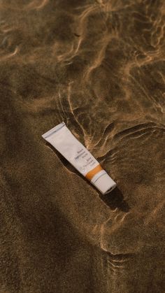 a tube of sunscreen sitting in the sand on top of a body of water