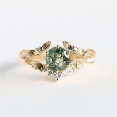 a gold ring with a green stone surrounded by leaves