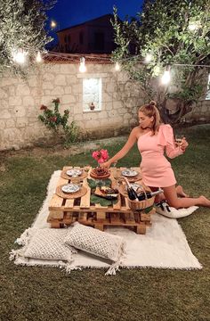 a woman sitting on the ground in front of a table full of food and drinks