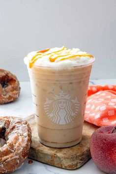 a cup of iced coffee next to two donuts and an apple on a cutting board