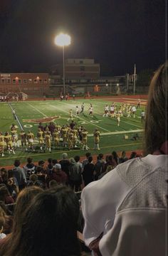 a football game is being played on the field at night with people watching from the bleachers