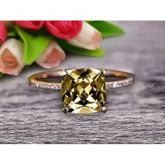 a yellow diamond ring sitting on top of a wooden table next to pink flowers and tulips