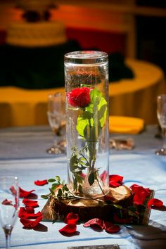 a vase filled with red roses sitting on top of a table next to wine glasses