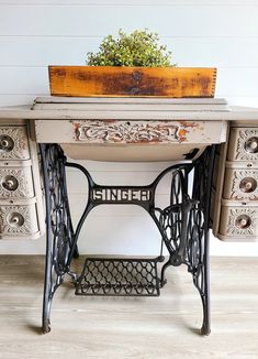 an old sewing machine sits on top of a table with drawers and a planter