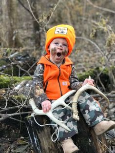 a small child sitting on top of a tree stump wearing an orange and black hat