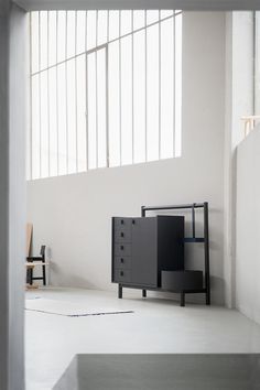 a black cabinet sitting on top of a white floor next to a chair and window