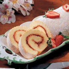 a roll with strawberries on it sitting on a plate next to some sliced strawberries