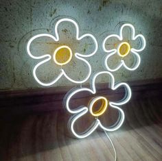 three flower shaped neon lights sitting on top of a wooden floor next to a wall