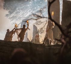 a group of people with torches in their hands standing on the ground next to some rocks