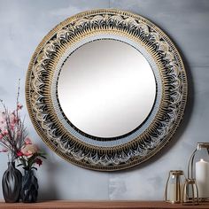 a round mirror sitting on top of a wooden table next to vases and flowers